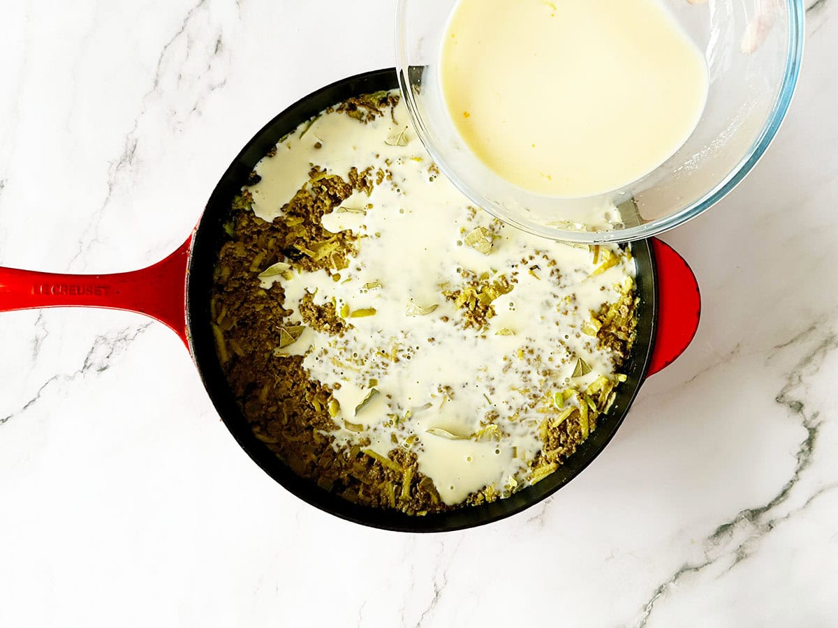 Custard poured evenly over bobotie in skillet before baking