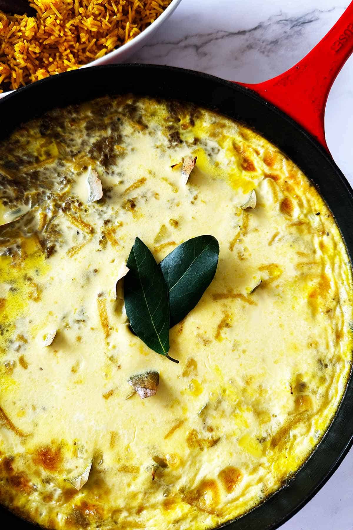Close-up of baked Cape Malay bobotie in skillet with yellow rice on side