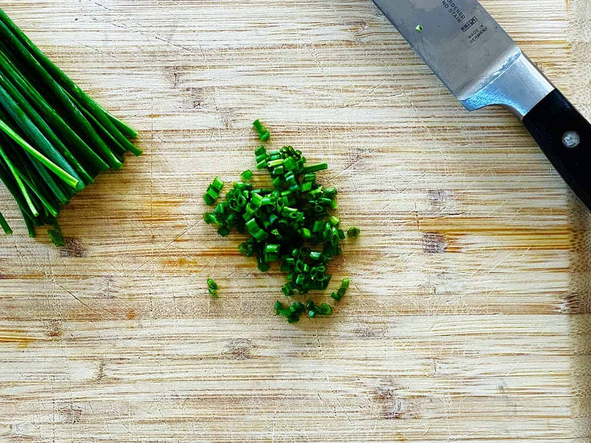 Fresh chives half chopped on board with chef’s knife.