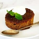 South African malva pudding on white plate topped with cream, soft caramelised sponge dessert