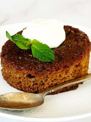 South African malva pudding on white plate topped with cream, soft caramelised sponge dessert
