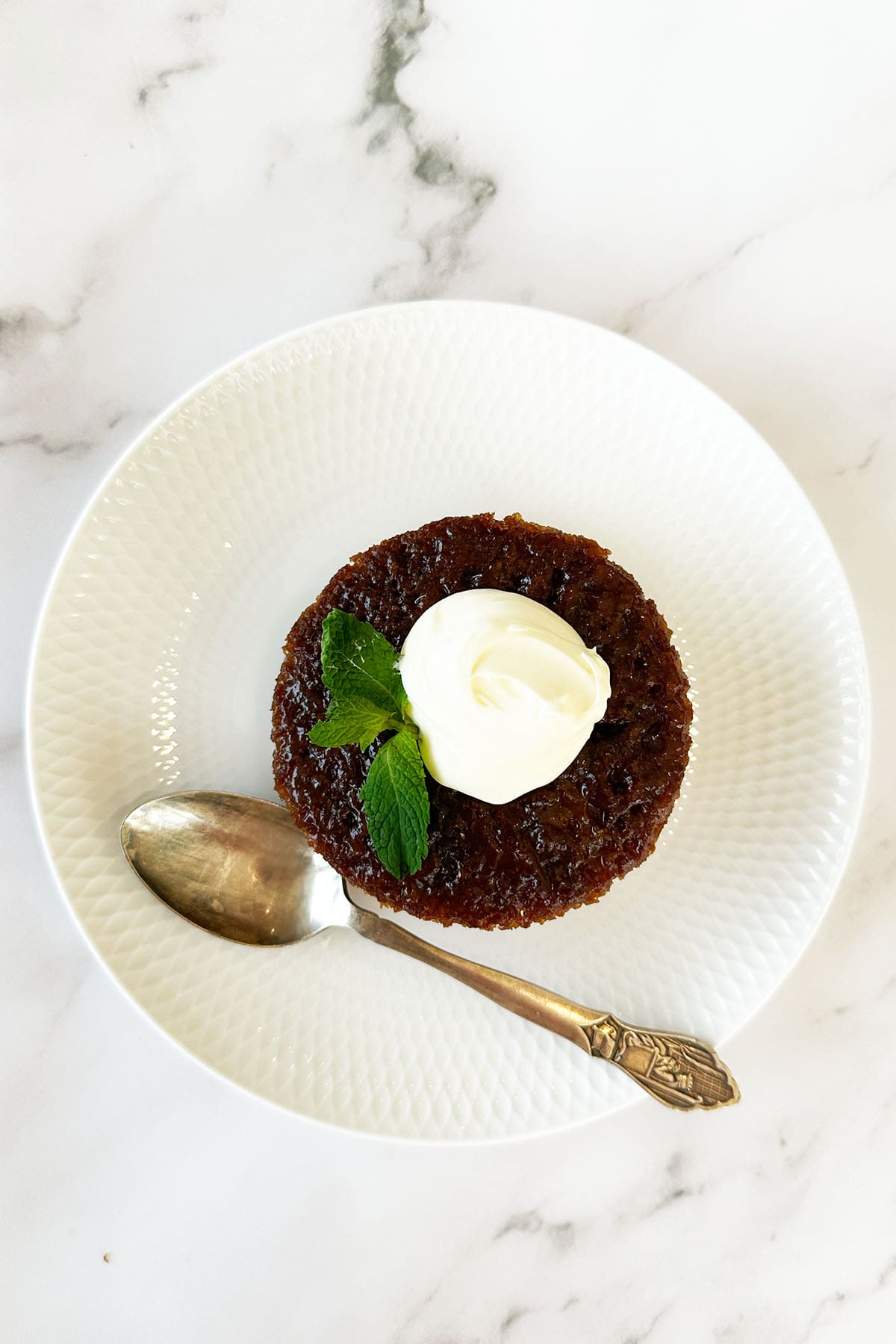 South African malva pudding on white plate topped with cream, soft caramelised sponge dessert