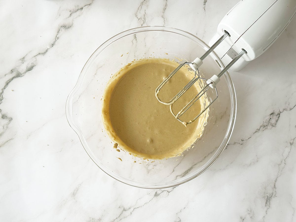 Apricot jam mixed into Malva pudding batter with hand mixer in glass bowl