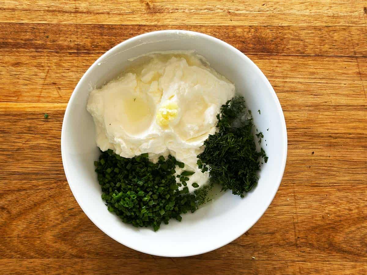 Yoghurt, chives, dill, garlic, and lemon juice in bowl.