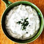 Greek yoghurt ranch dip in green bowl on wooden board.