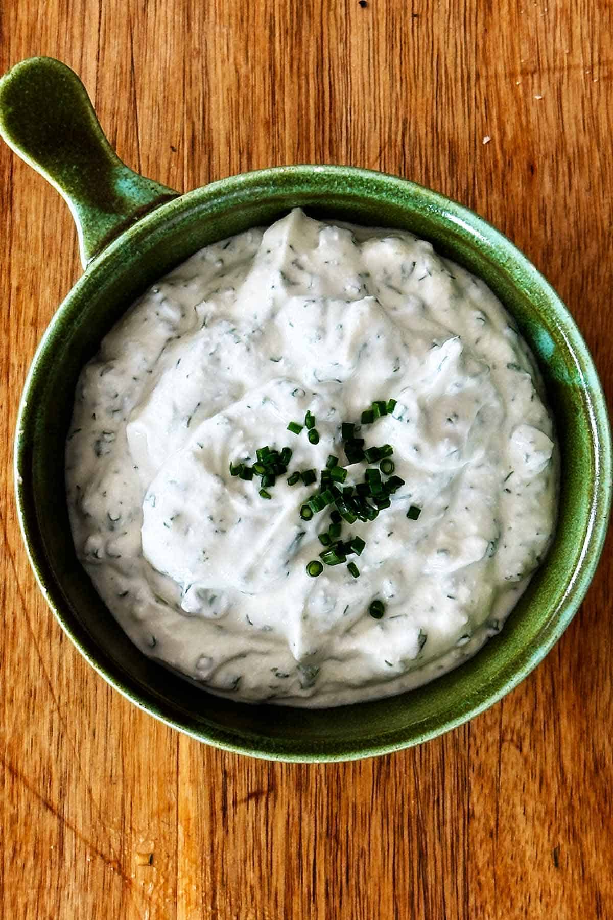 Greek yoghurt ranch dip in green bowl on wooden board.