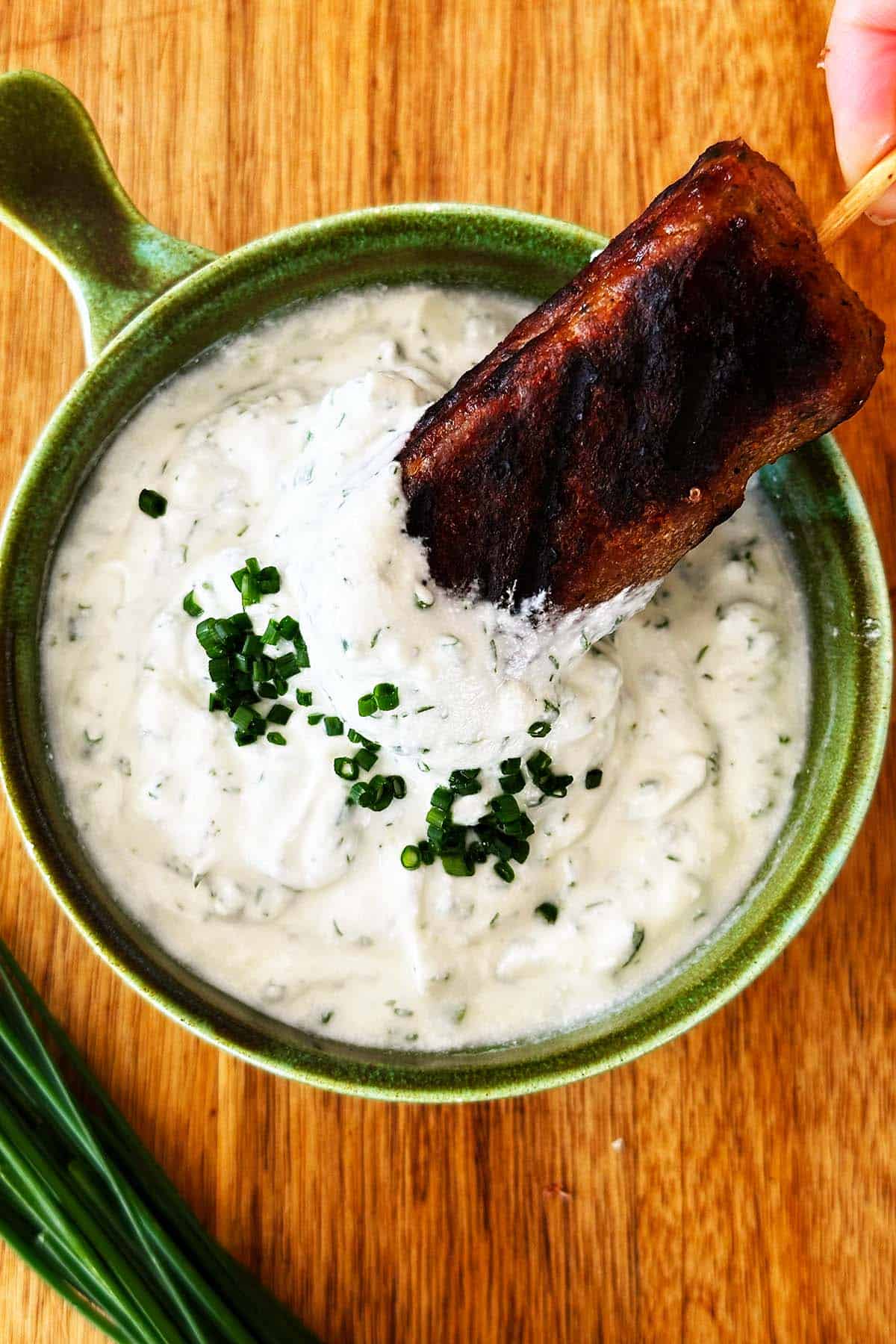 Lamb kofta dipped into Greek yoghurt ranch dip in green bowl.