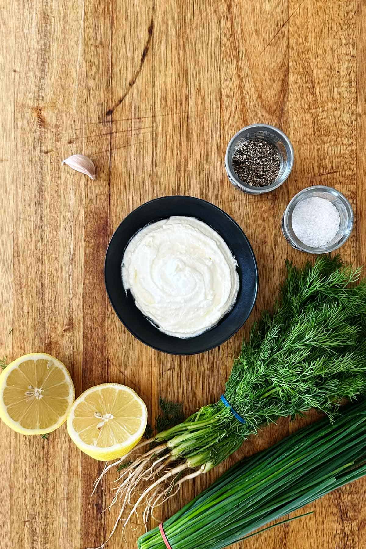 Greek yoghurt ranch dip ingredients on wooden board, chives, dill, lemon.