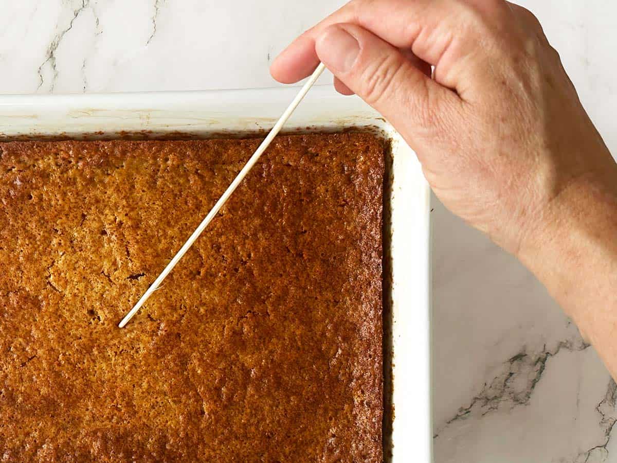 Poking holes in hot Malva pudding with wooden skewer after baking