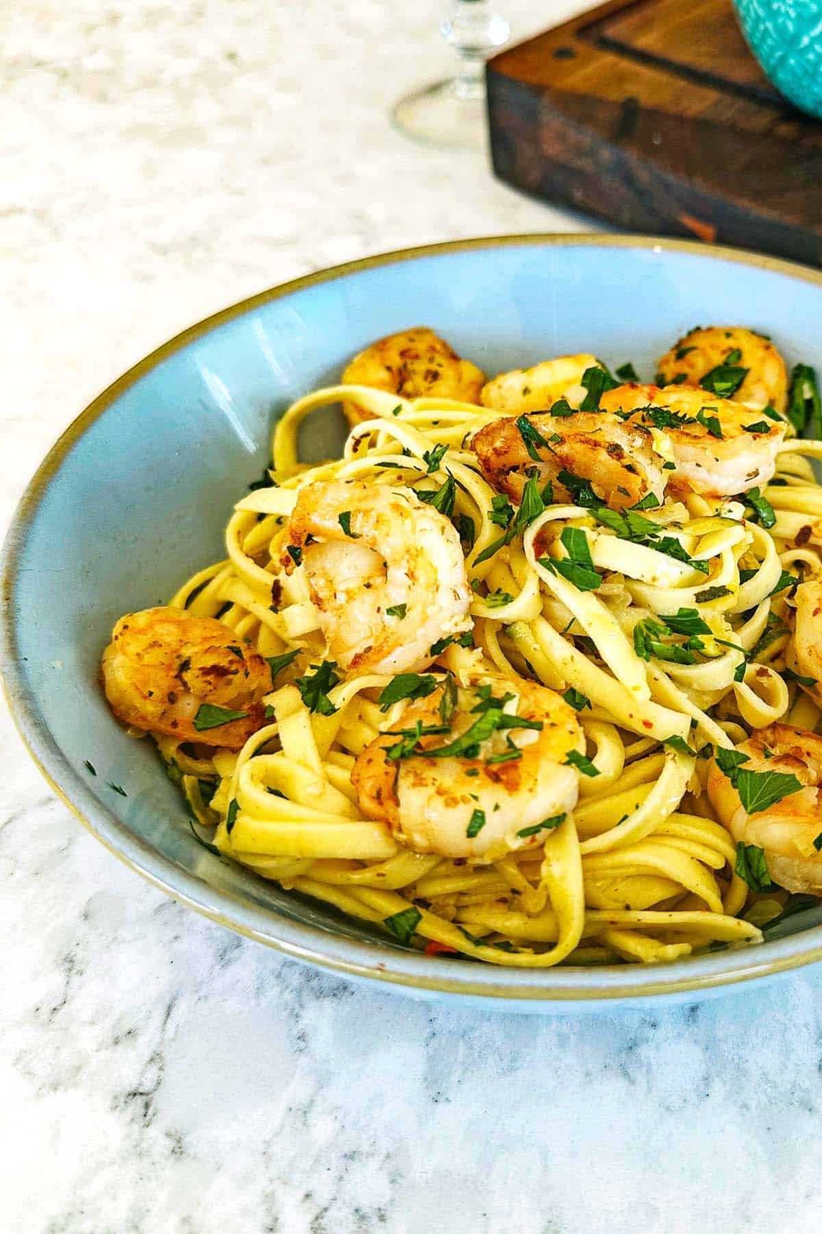 Courgette prawn pasta, served in a blue bowl with caramelised prawns, courgette, and parsley.