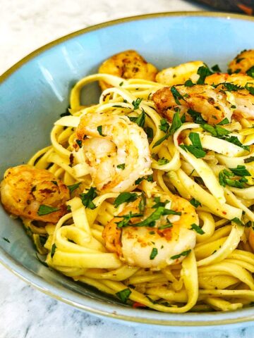 Courgette prawn pasta, served in a blue bowl with caramelised prawns, courgette, and parsley.