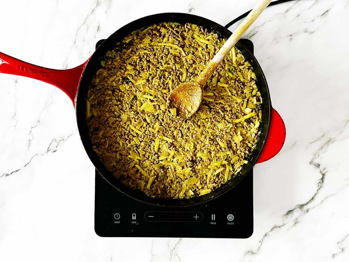 Smoothing bobotie mince evenly in skillet ready for custard topping