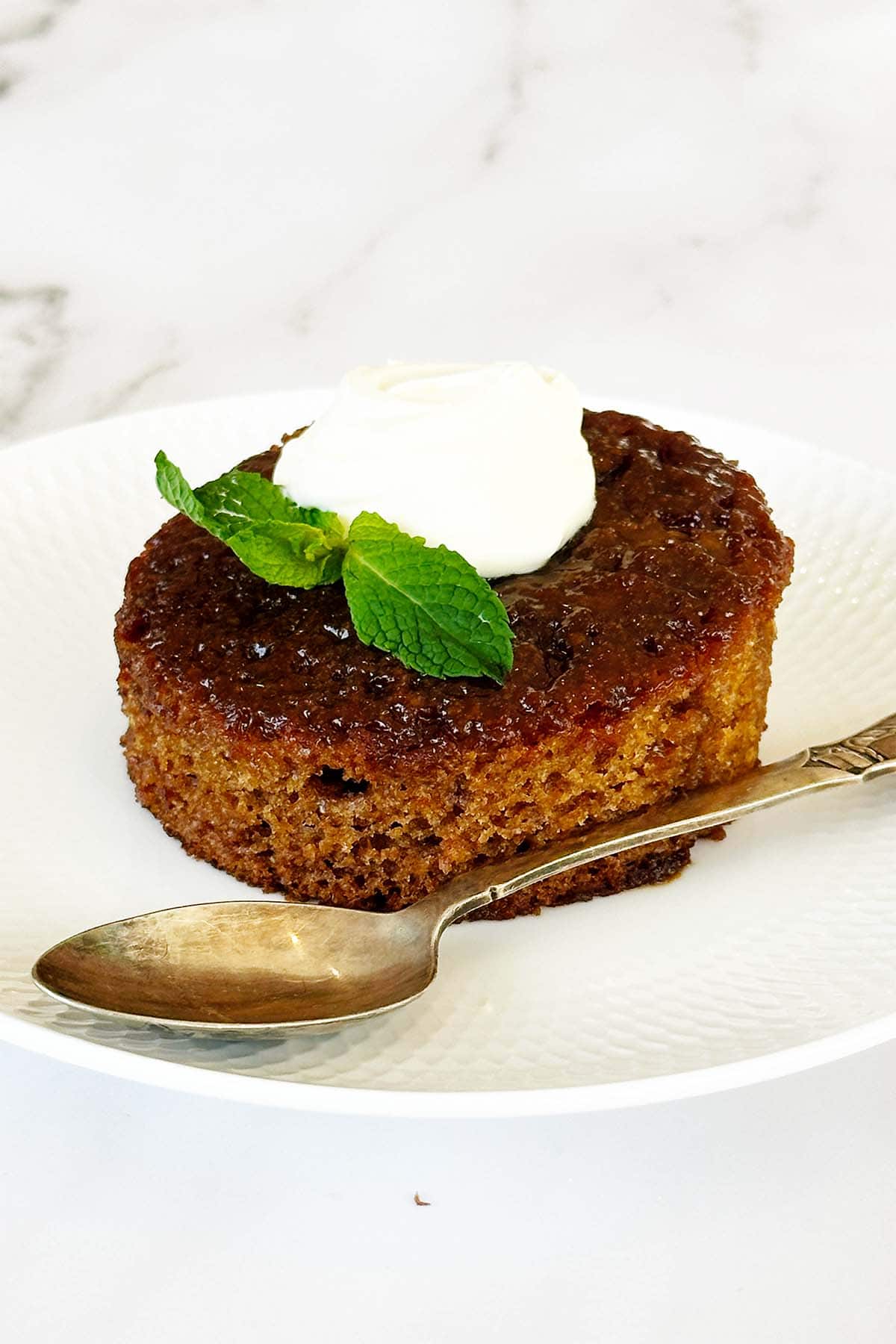 South African malva pudding on white plate topped with cream, soft caramelised sponge dessert