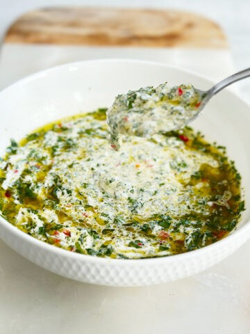 Bowl of chimichurri mayo with spoon scooping creamy sauce on marble board