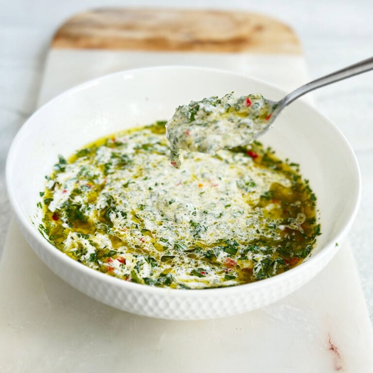 Bowl of chimichurri mayo with spoon scooping creamy sauce on marble board