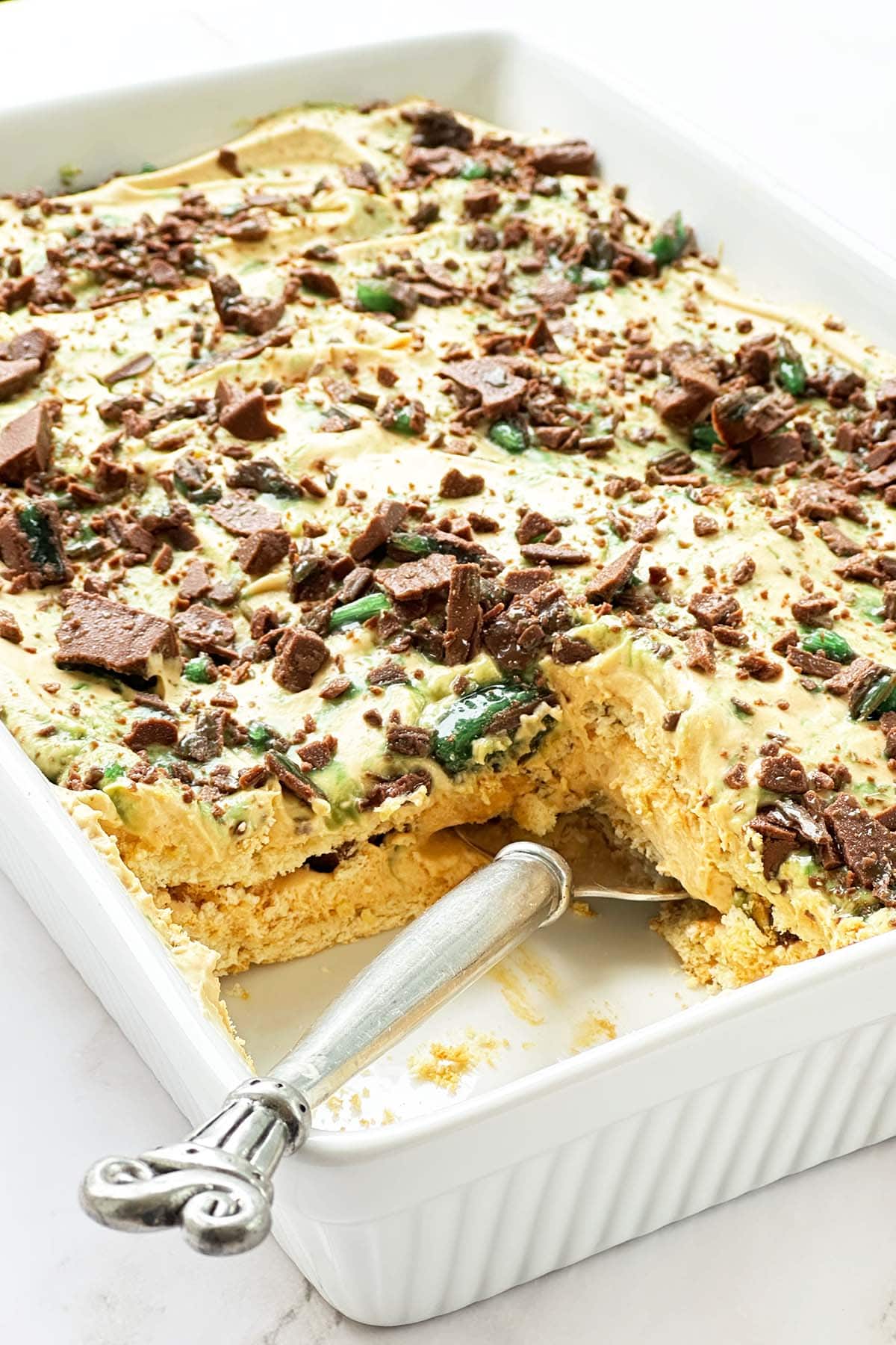 Peppermint crisp tart in a white dish with one slice removed showing caramel cream and mint chocolate layers