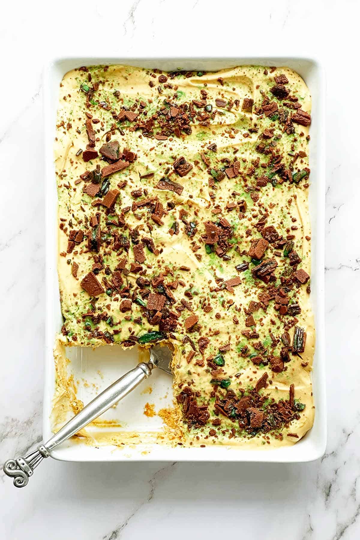 Top view of peppermint crisp tart in a white dish with a slice removed and cake lifter