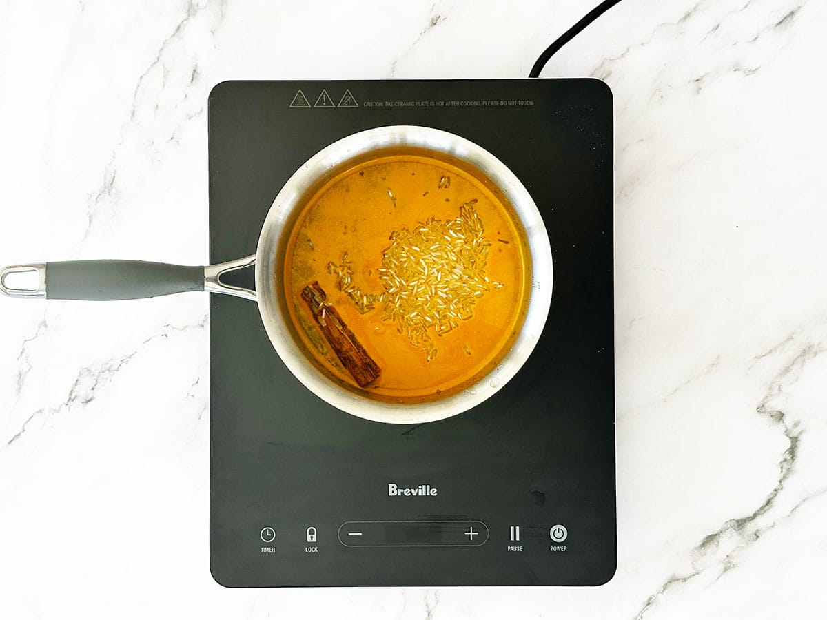 how to make a yellow rice - Adding rice to pot with turmeric, sugar, salt and cinnamon in water