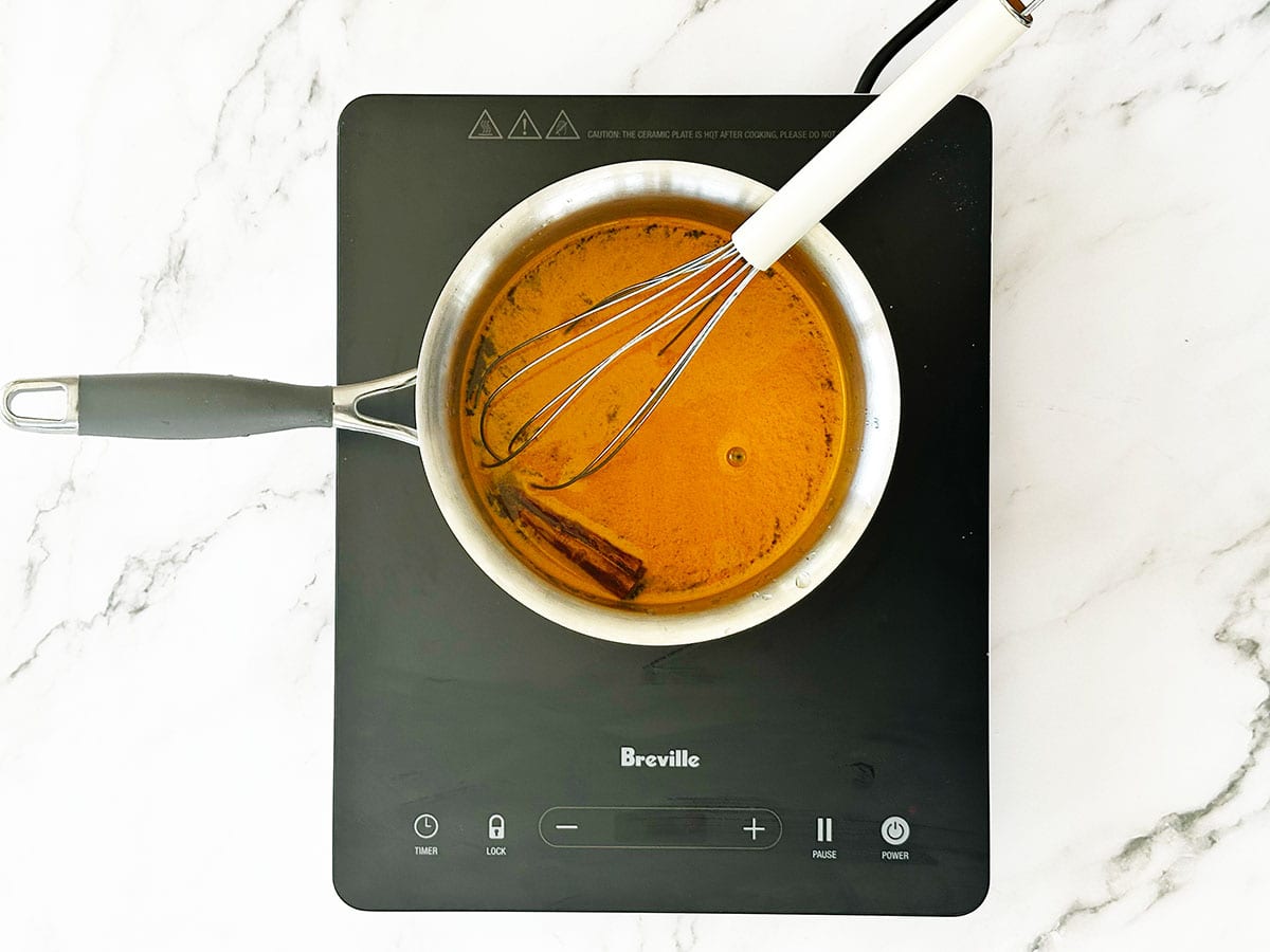 how to make yellow rice - Adding turmeric, sugar, salt and cinnamon stick to water in pot