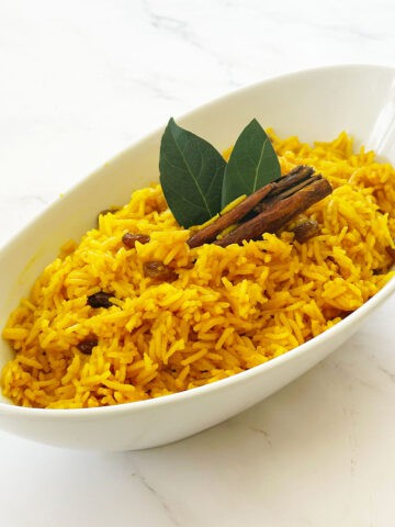 South African yellow rice (geelrys) with raisins in white bowl with cinnamon stick