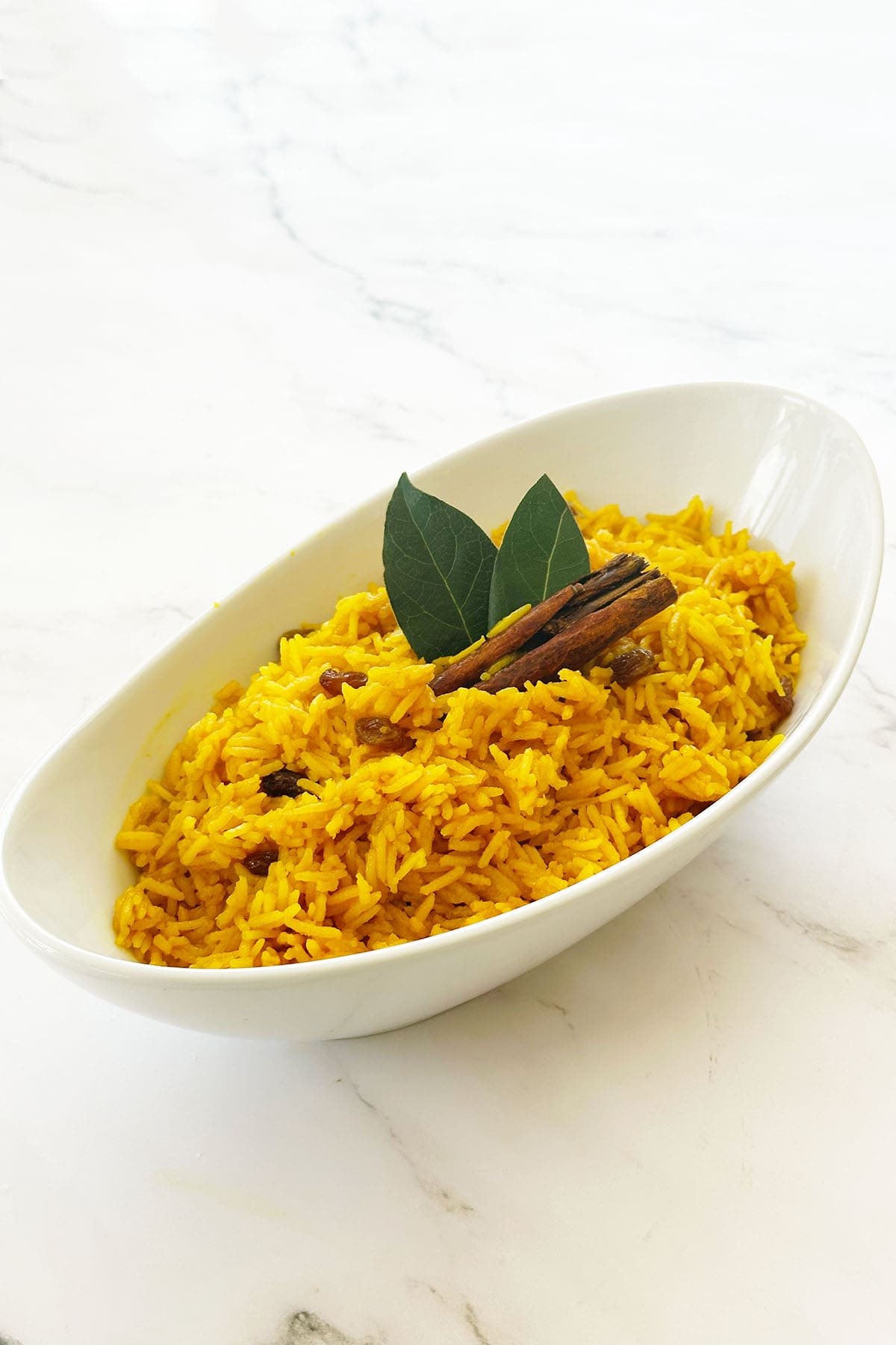 South African yellow rice (geelrys) with raisins in white bowl with cinnamon stick