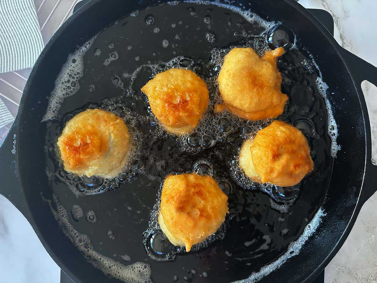 Five golden brown vetkoeke being deep fried to perfection